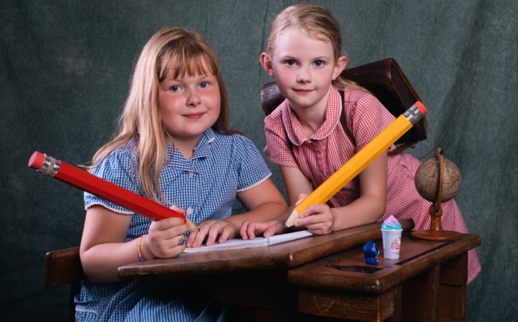 dwie dziewczynki stoją przy szkolnej ławce z dużymi ołówkami