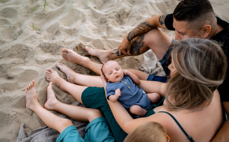cała rodzina pozuje z malutkim dzieckiem na piasku