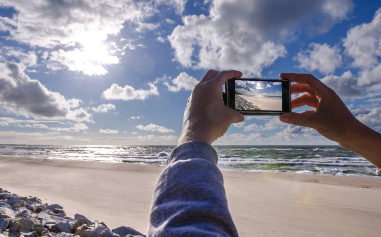 Osoba, która robi zdjęcie nieba, wody i piasku smartfonem