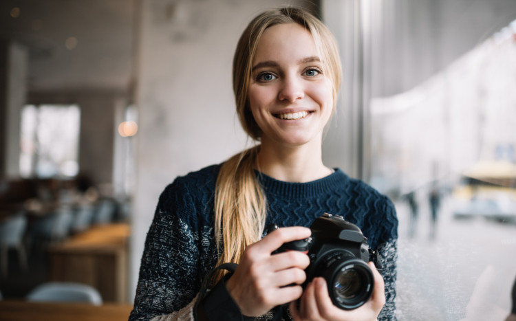 Uśmiechnięta fotografka o blond włosach i aparatem w rękach