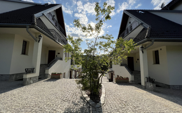 Dwa budynki, w których znajdują się pokoje dla Gości. Między budynkami rośnie zielone drzewko.
