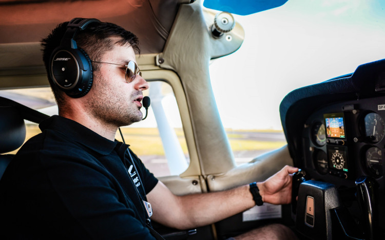 Mężczyzna w okularach przeciwsłonecznych w awionetce rozmawiający do słuchawki lotniczej