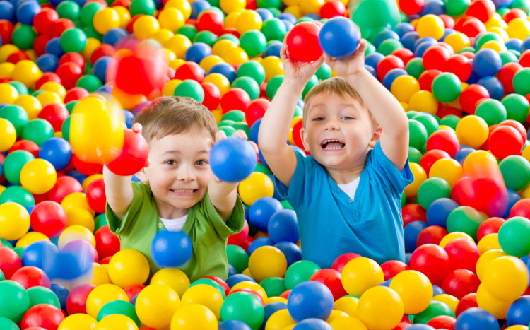 Dwóch radosnych chłopców siedzących z basenie z kulek plastikowych i trzymających kulki w ręce
