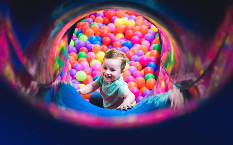 Uśmiechnięty chłopczyk zjeżdżający zjeżdżalnią do plastikowych i kolorowych kulek
