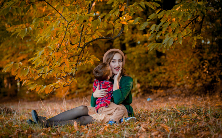 Kobieta z dzieckiem pozuje siedząc na jesiennych liściach