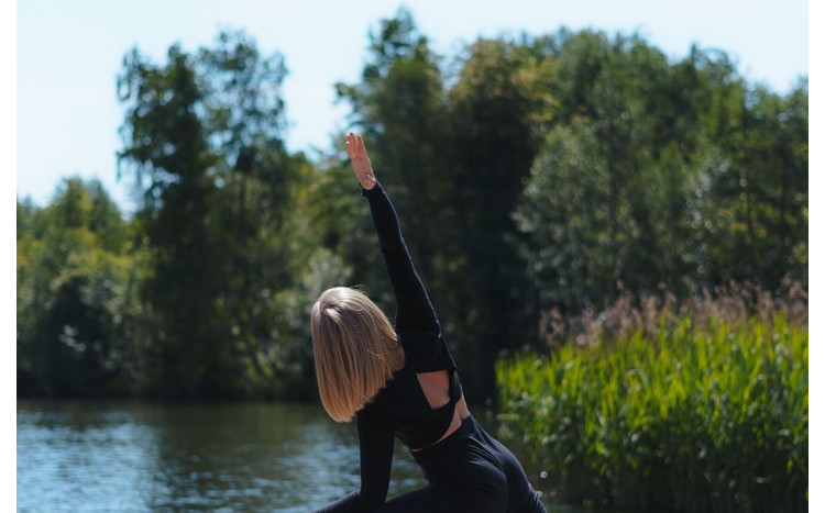 Kobieta w czarnym ubraniu praktykuje jogę wśród natury tuż nad jeziorem