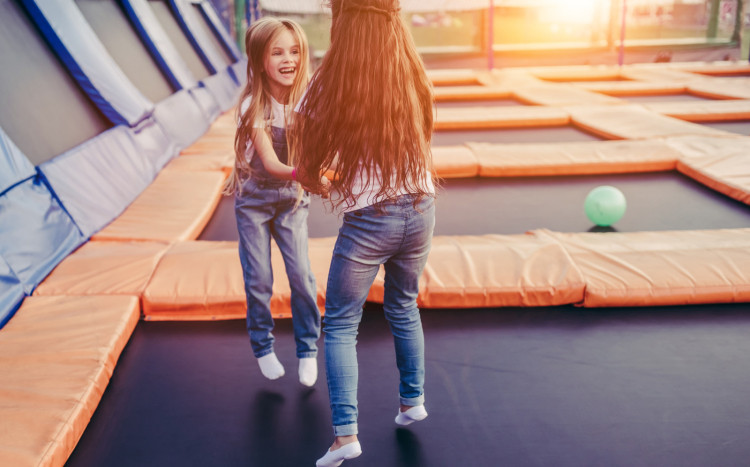 Dwie dziewczynki trzymające się za ręce w długich włosach skaczące na trampolinie w parku trampolin
