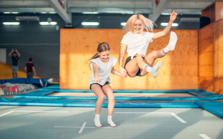 Kobieta skacząca z nogami w górze i dziewczynka skacząca prosto w parku trampolin