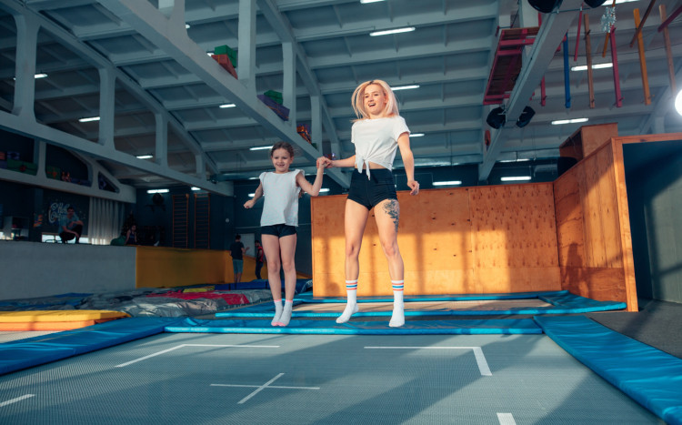 Radosna kobieta i dziewczynka skaczące wysoko na trampolinach w parku trampolin