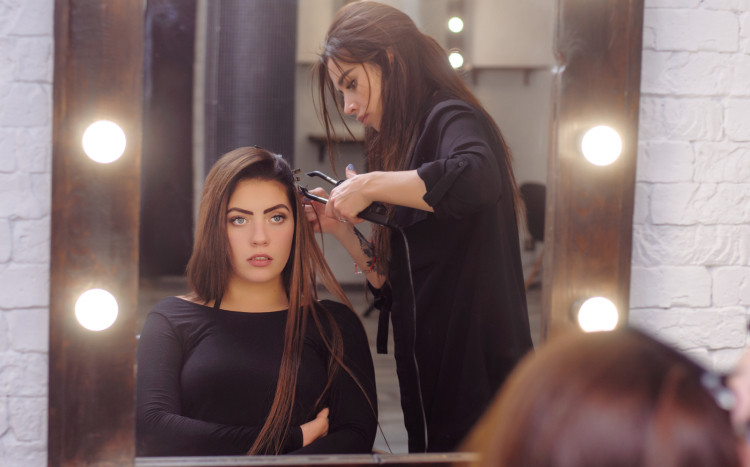 Kobieta przygląda się w lustrze, podczas gdy fryzjerka przedłuża jej włosy