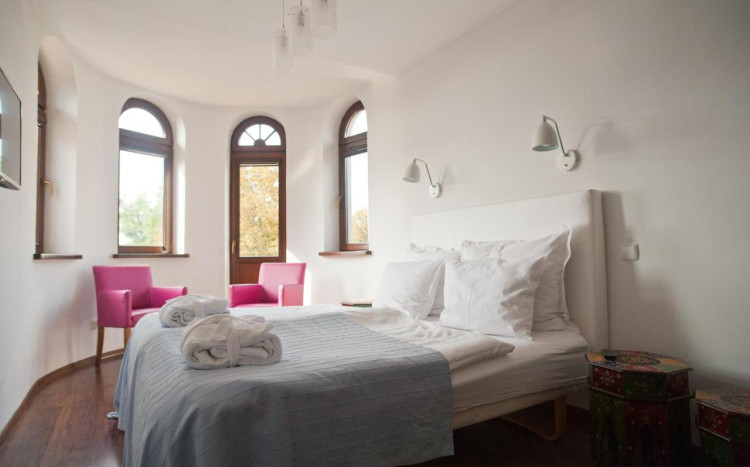 Duże łóżko dwuosobowe ze szlafrokami na nim oraz różowymi fotelami