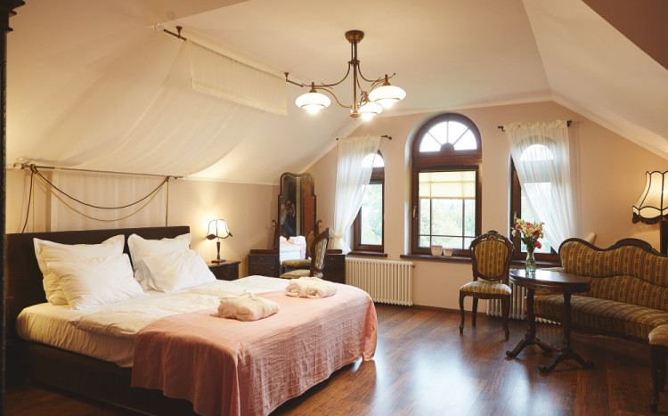 Sypialnia urządzona w bardzo ciepłym wystroju z dużym łóżkiem dwuosobowym oraz starodawnymi krzesłami