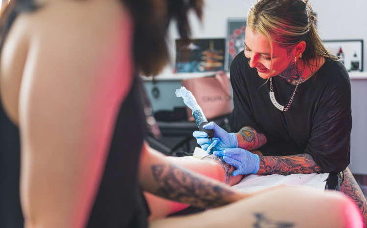 Wesoła tatuatorka wykonująca tatuaż na nodze dziewczyny