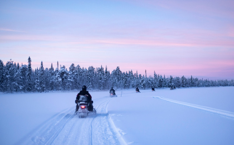 Pięć osób jadących na skuterach śnieżnych przez teren pokryty śniegiem
