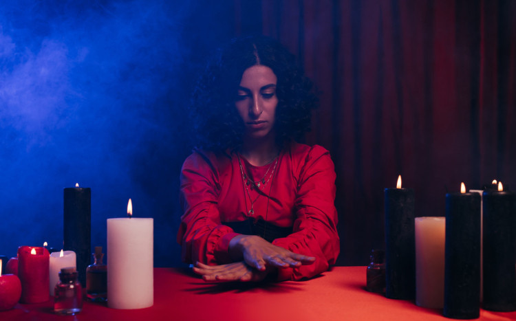 Kobieta w czerwonej bluzce ze skrzyżowanymi rękami wśród świec
