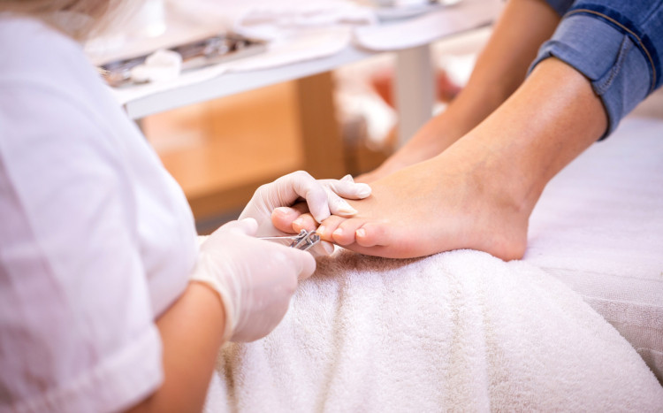Kosmetolog w rękawiczkach ochronnych skraca obcinaczką paznokcie u stóp