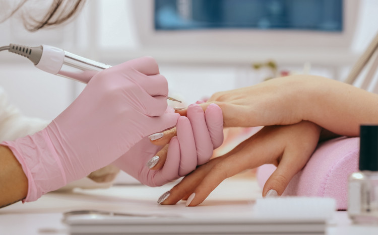 Dłonie w różowych rękawiczkach frezują skórki u dłoni swojej klientki