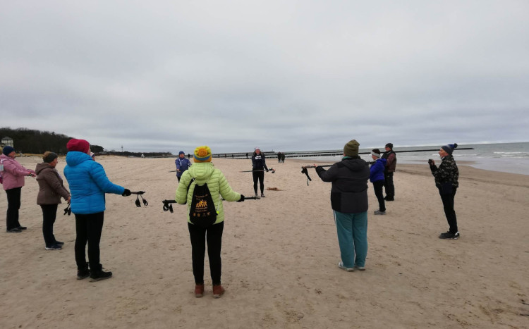 Grupa osób podnosząca kijek od nordic walking w ramach rozgrzewki