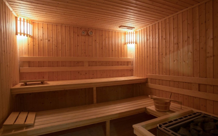 Drewniana sauna z koszykiem z kamieniami oraz żółtym światłem w Pomorze Health & Family Resort