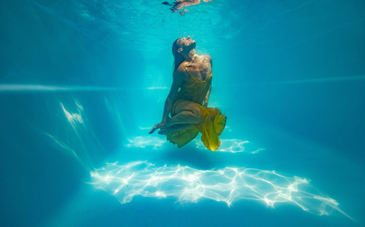 Kobieta w żółtej sukience pozująca do zdjęcia pod wodą w basenie