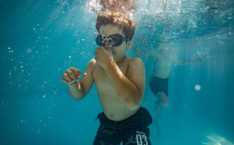 Chłopiec w okularach podwodnych zatykający nos w wodzie w basenie