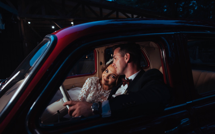 Panna młoda w białej sukni oparta na ramieniu męża w samochodzie