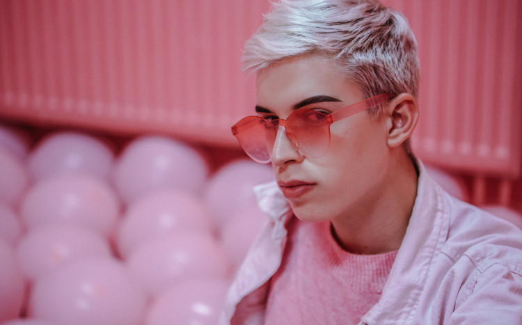 Chłopak w różowych okularach pozujący na różowym tle z różowymi balonami