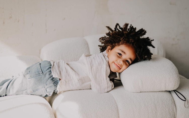Chłopczyk w afro leżący na łóżku i pozujący do zdjęcia z uśmiechem
