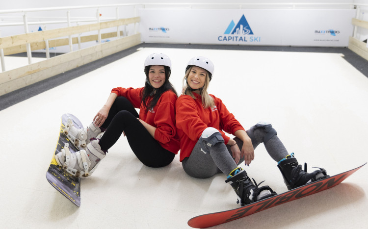 Dwie radosne dziewczyny w kaskach, ochraniaczach na kolana i deskach snowboardowych na hali Capital Ski