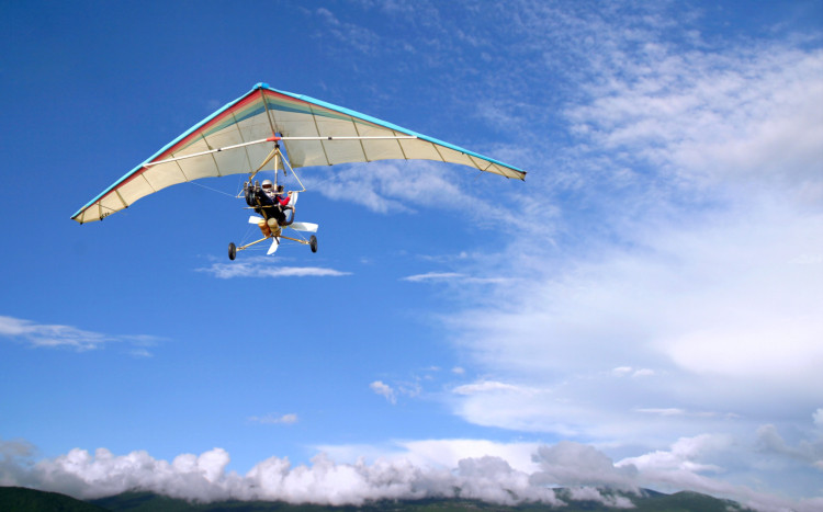 Osoba lecąca na motolotni z białym skrzydłem na tle niebieskiego nieba