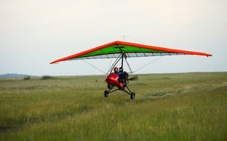 Czerwona dwuosobowa motolotnia startująca z zielonej łąki