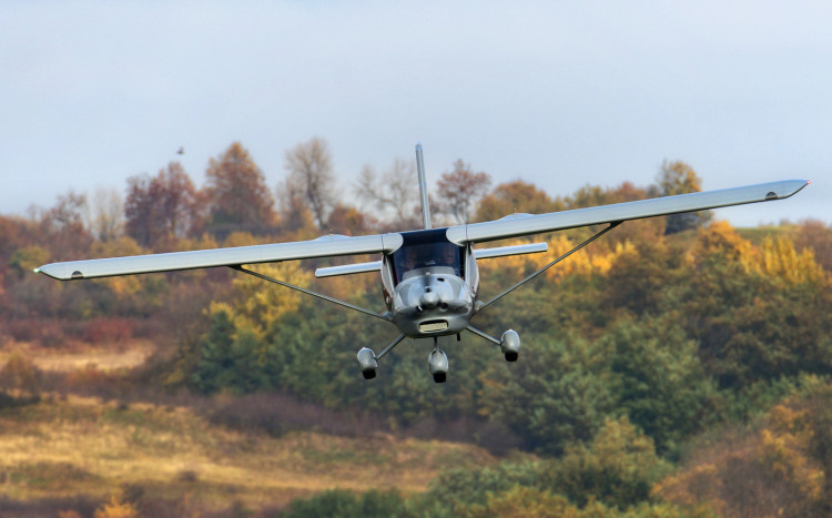 Srebrny samolot ultralekki lecący na tle jesiennych drzew