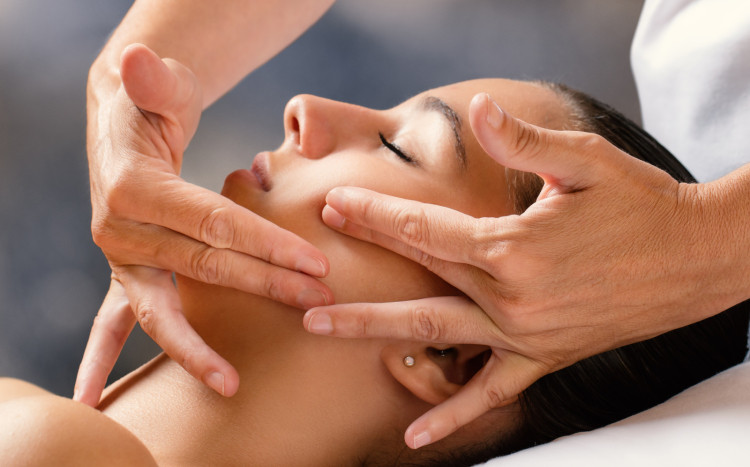 Dłonie wykonujące masaż Kobido na twarzy kobiety