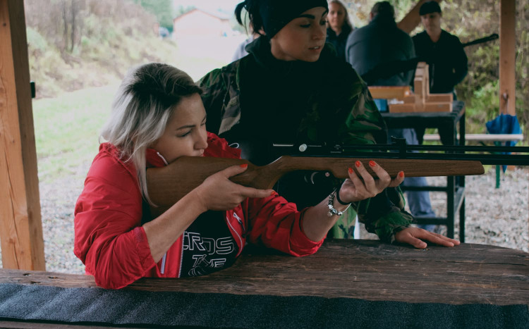 Kobieta w czerwonej kurtce celująca pistoletem do celu, obok niej instruktorka