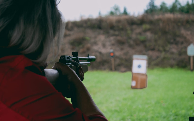 Kobieta w czerwonej kurtce celująca do tarczy z pistoletu na strzelnicy