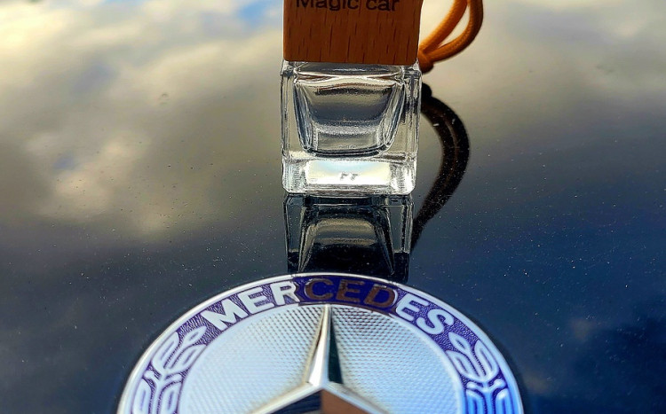 Zapach do auta w buteleczce z drewnianym korkiem leżący obok znaczku samochodowego z Logo Mercedes-Benz