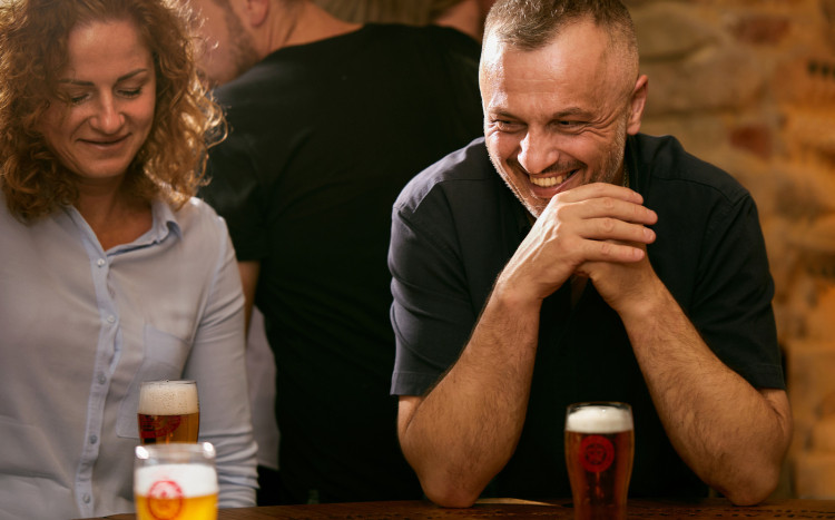 Szczęśliwy mężczyzna podpierający głowę rękami oraz kobieta obok siedzą przy piwie podczas jego degustacji