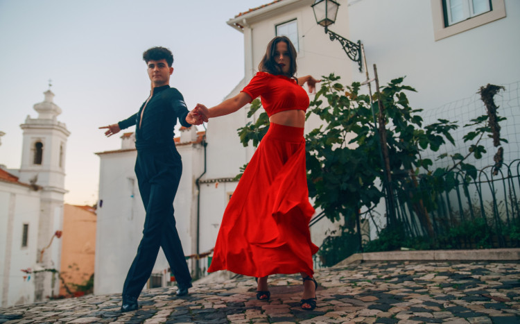 Kobieta w długiej czerwonej sukni i mężczyzna w garniturze tańczą taniec latynoski na cichej ulicy starego miasta w starożytnej,