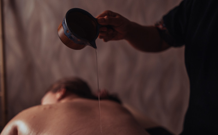 Masażystka wylewająca olejek na plecy kobiety leżącej na brzuchu