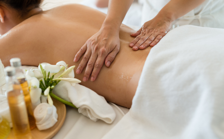 Masażystka wsmarowująca olejek w plecy kobiety podczas masażu