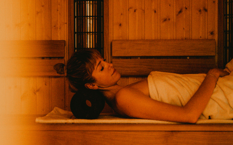 Kobieta owinięta w biały ręcznik leżąca na plecach podczas seansu w saunie Infrared
