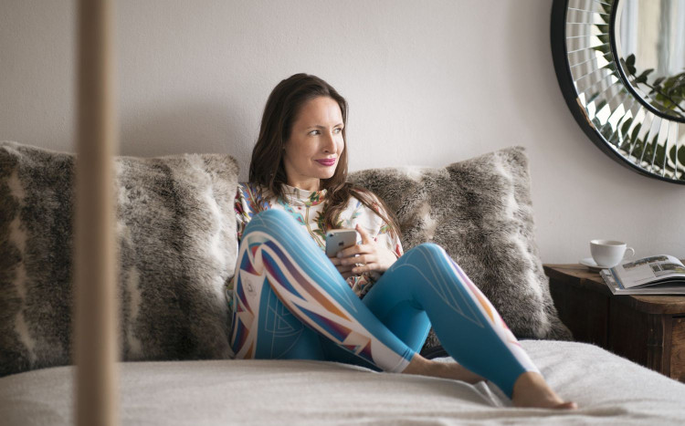 Kobieta siedząca na łóżku w kolorowych legginsach i z telefonem w rękach