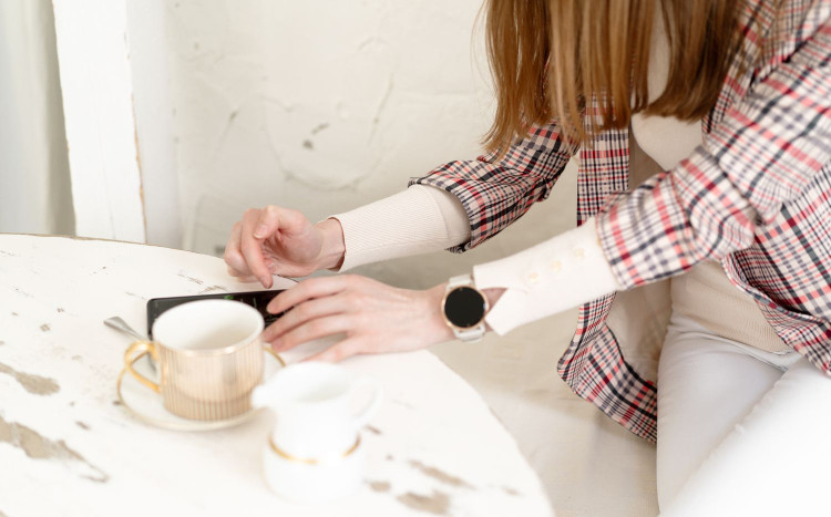 Kobieta korzystająca ze smartfona, obok niej filiżanka kawy