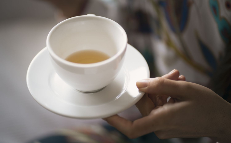 Damska dłoń trzymająca filiżankę z herbatą na dnie