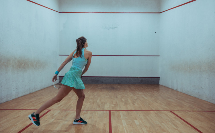 Dziewczyna w niebieskim stroju uderzająca piłka o ścianę podczas gry w squasha