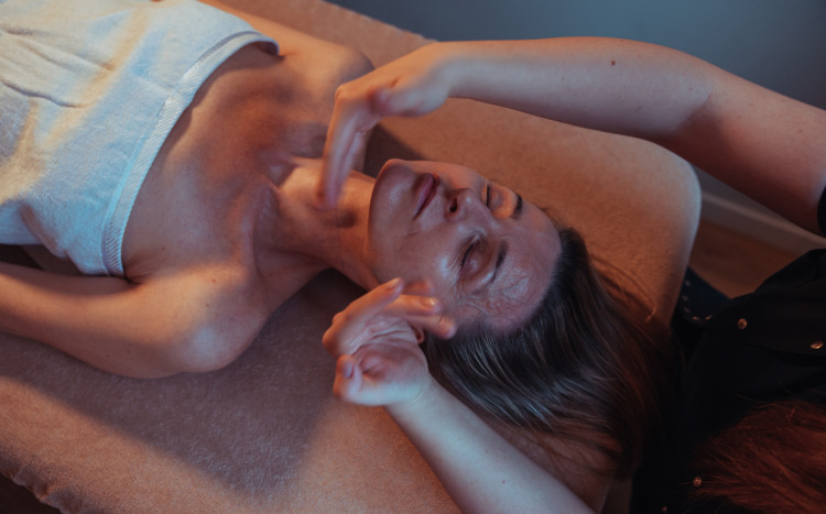 Kobieta leżąca na plecach w białym ręczniku podczas masażu twarzy