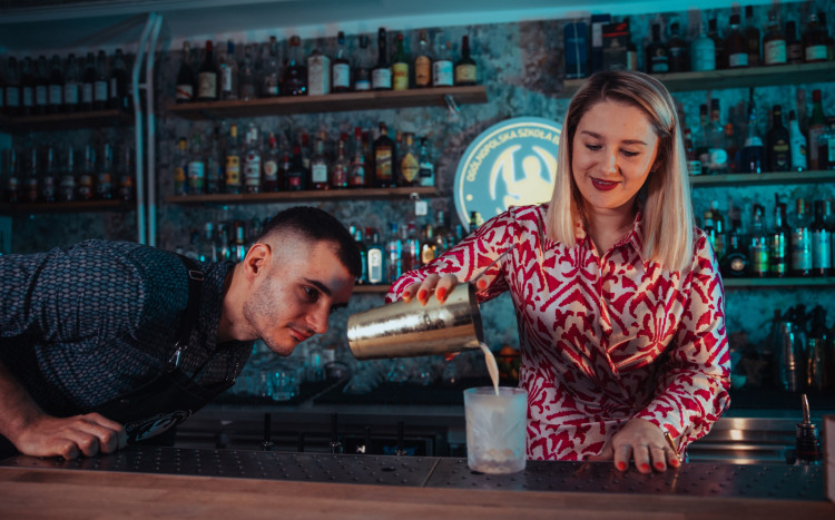 Barmanka przelewająca drinka do szklanki, obok przyglądający się kursant