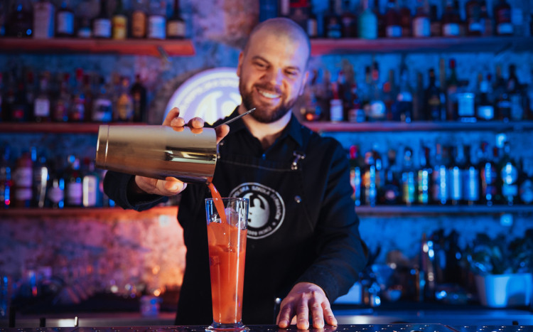 Barman wlewający pomarańczowy napój z shakera do wysokiej szklanki