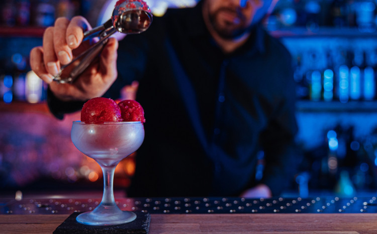 Barman przyozdabiający miętą kulki czerwonych lodów w pucharku