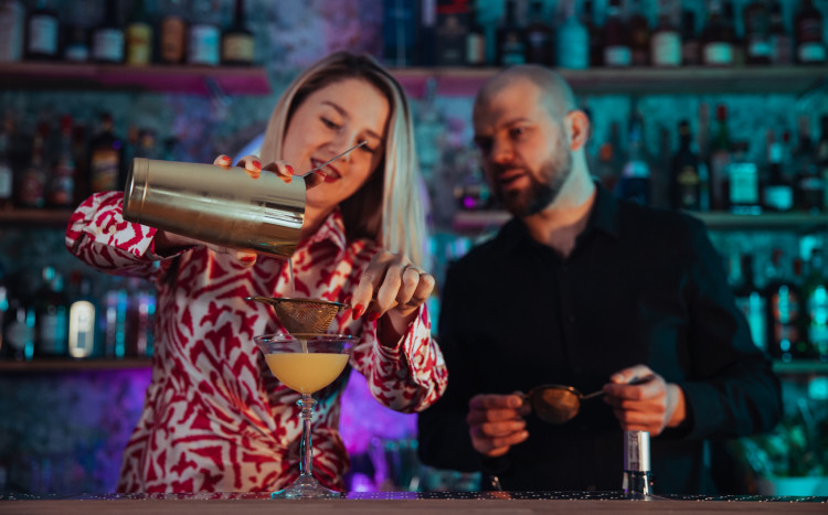 Barmanka pokazująca mężczyźnie, jak przelewać gotowy koktajl przez sitko
